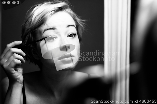 Image of Woman getting ready for work doing morning makeup routine applying mascara in bathroom mirror at home. Beautiful caucasian girl applying eye make-up. Black and white image