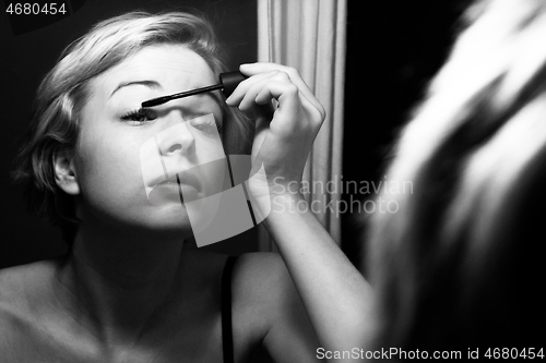 Image of Woman getting ready for work doing morning makeup routine applying mascara in bathroom mirror at home. Beautiful caucasian girl applying eye make-up. Black and white image