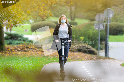 Image of Casual caucasian teenager wearing protective face mask riding urban electric scooter in city park during covid pandemic. Urban mobility concept