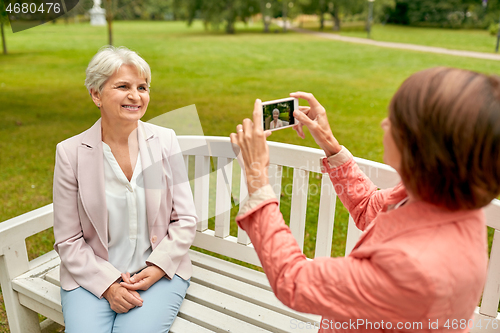 Image of senior woman photographing her friend at park