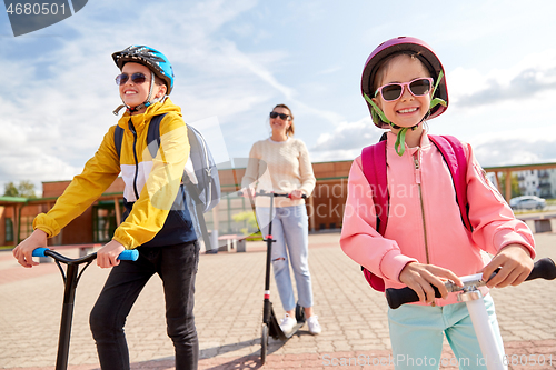 Image of happy school children with mother riding scooters