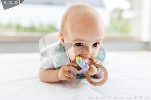 Image of baby girl on white blanket chewing wooden rattle