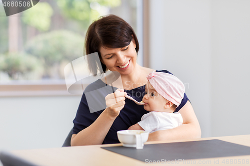 Image of middle-aged mother feeding baby daughter at home