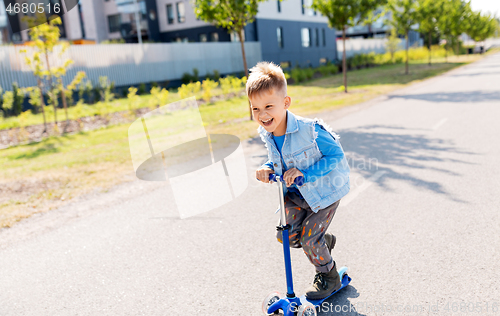 Image of happy little boy riding scooter in city