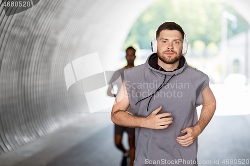Image of male friends with headphones running outdoors