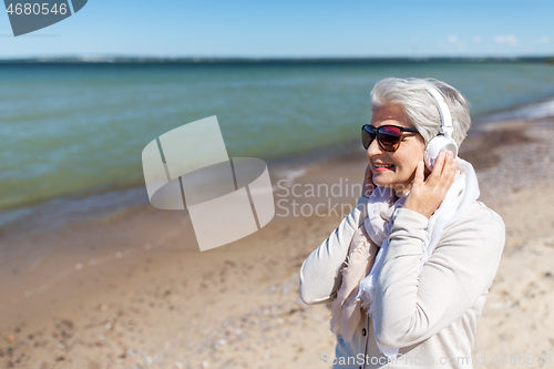 Image of old woman in headphones listens to music on beach