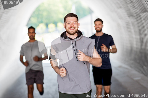 Image of male friends with earphones running outdoors