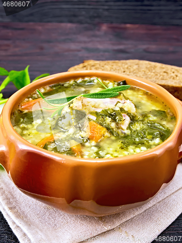 Image of Soup with couscous and spinach in clay bowl on dark board