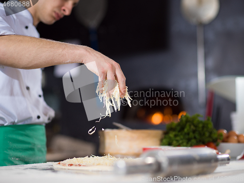 Image of chef sprinkling cheese over fresh pizza dough