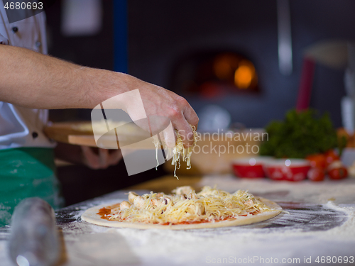 Image of chef sprinkling cheese over fresh pizza dough