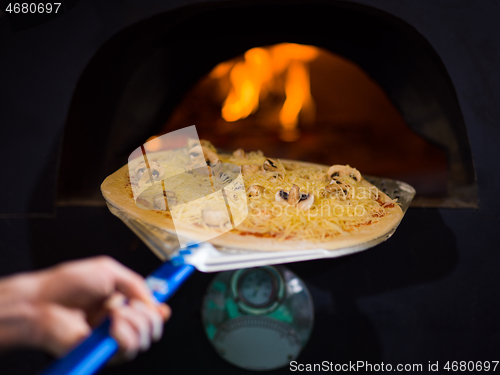 Image of chef putting delicious pizza to brick wood oven