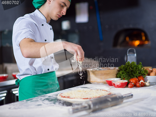 Image of chef sprinkling cheese over fresh pizza dough