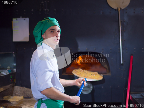 Image of chef putting delicious pizza to brick wood oven