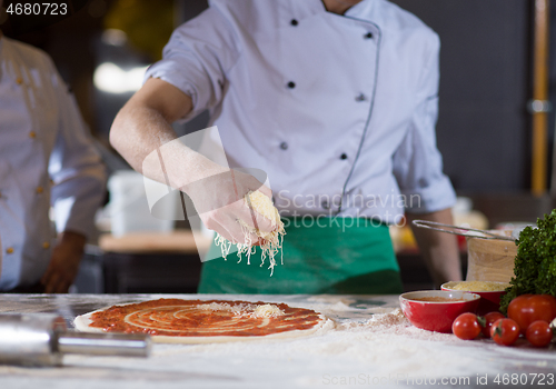 Image of chef sprinkling cheese over fresh pizza dough