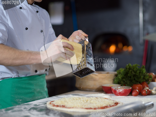 Image of chef sprinkling cheese over fresh pizza dough