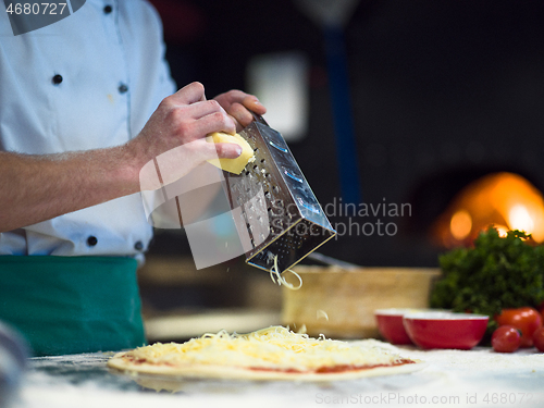 Image of chef sprinkling cheese over fresh pizza dough