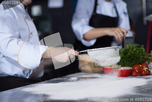 Image of chef sprinkling flour over fresh pizza dough