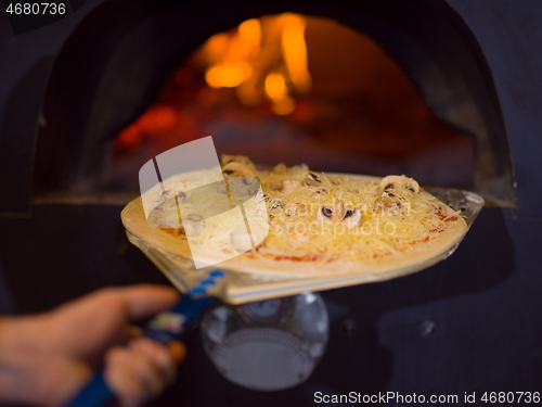 Image of chef putting delicious pizza to brick wood oven