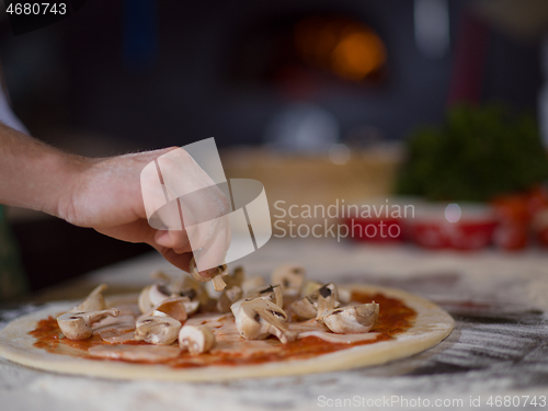 Image of chef putting fresh mushrooms on pizza dough