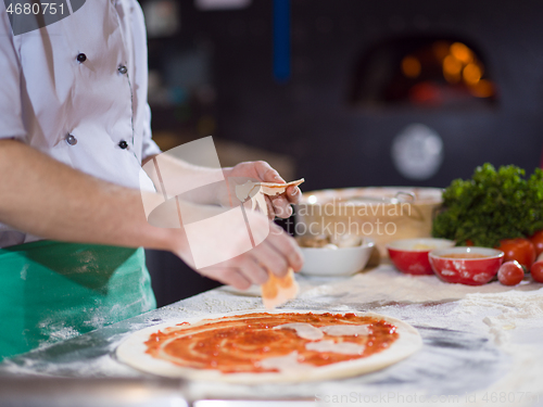 Image of chef putting cut sausage or ham on pizza dough