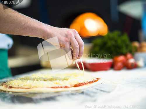 Image of chef sprinkling cheese over fresh pizza dough