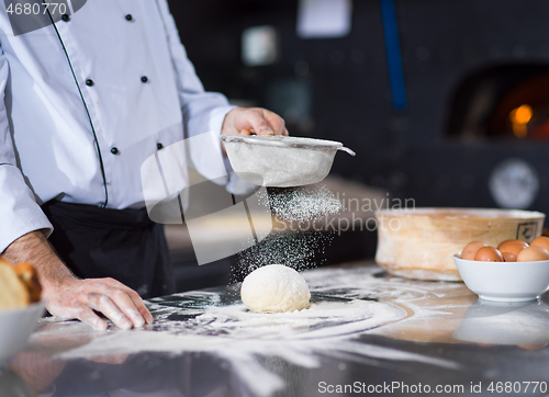 Image of chef sprinkling flour over fresh pizza dough