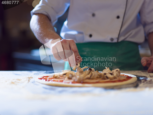 Image of chef putting fresh mushrooms on pizza dough