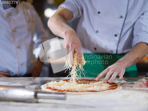 Image of chef sprinkling cheese over fresh pizza dough