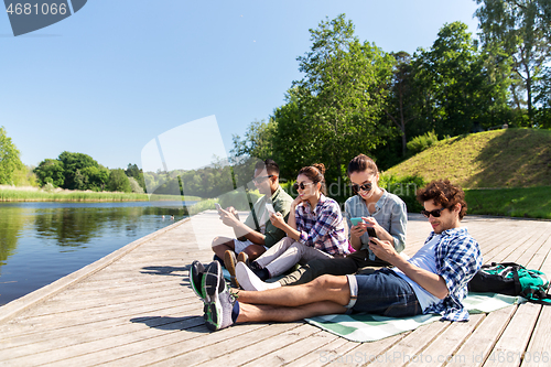 Image of friends with smartphone on lake pier in summer