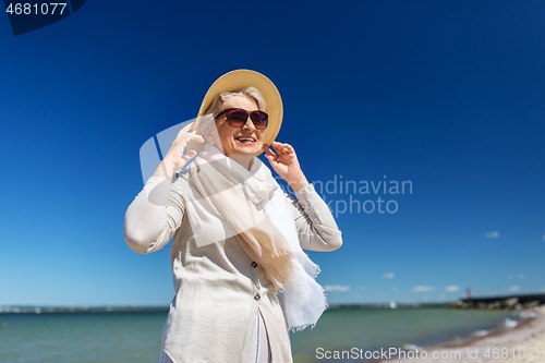 Image of happy senior woman in sunglasses and hat on beach