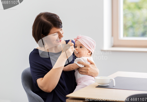 Image of middle-aged mother feeding baby daughter at home