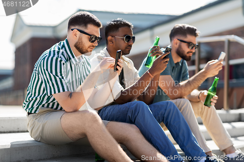 Image of men with smartphones drinking beer on street