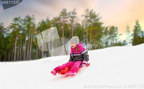 Image of happy little girl sliding down on sled in winter