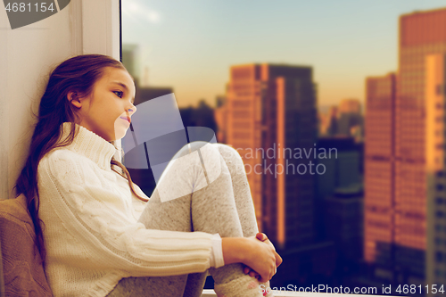 Image of sad girl sitting on sill at home window over city