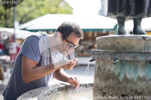 Image of Thirsty young casual cucasian man drinking water from public city fountain on a hot summer day