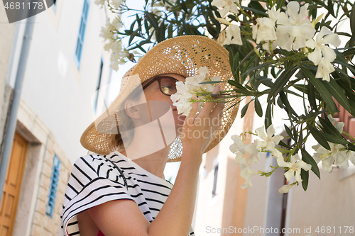 Image of Beautiful young caucasian woman smelling white flowers on the street of traditional old Mediterranean costal town