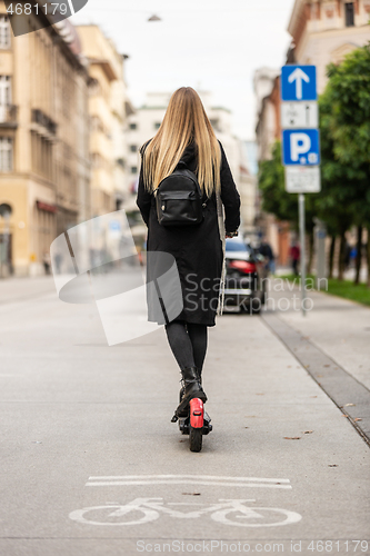 Image of Rear view of girl riding public rental electric scooter in urban city environment. New eco-friendly modern public city transport in Ljubljana