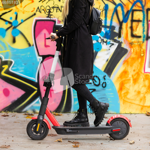 Image of Trendy teenage girl riding public rental electric scooter in urban city environment at fall. New eco-friendly modern public city transport in Ljubljana