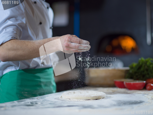 Image of chef sprinkling flour over fresh pizza dough