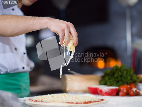 Image of chef sprinkling cheese over fresh pizza dough