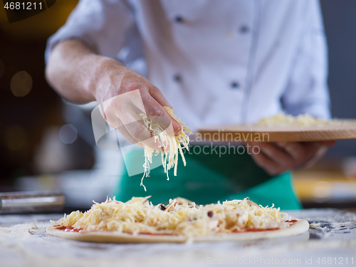 Image of chef sprinkling cheese over fresh pizza dough