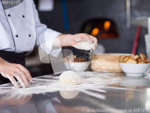 Image of chef sprinkling flour over fresh pizza dough