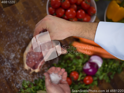 Image of Chef putting salt on juicy slice of raw steak