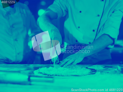 Image of chef sprinkling cheese over fresh pizza dough