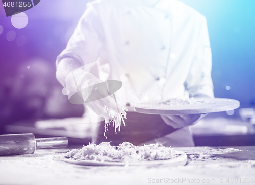 Image of chef sprinkling cheese over fresh pizza dough