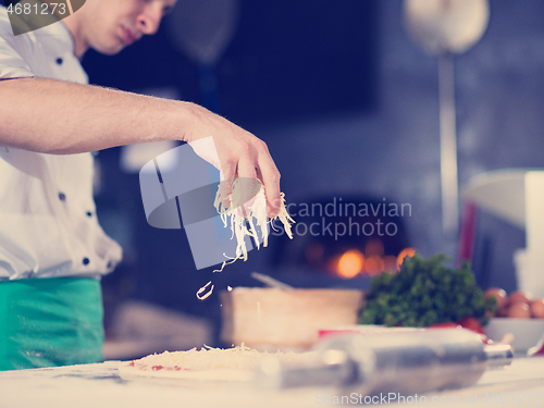 Image of chef sprinkling cheese over fresh pizza dough