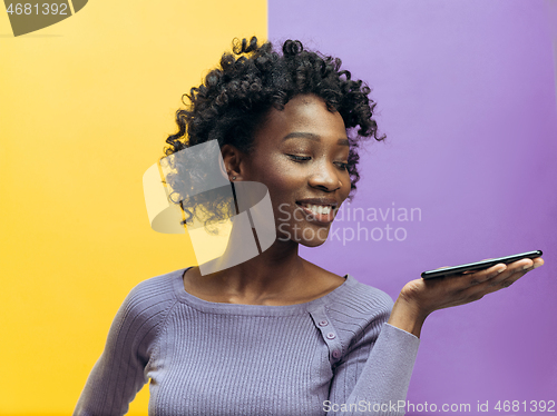 Image of Indoor portrait of attractive young black woman holding blank smartphone