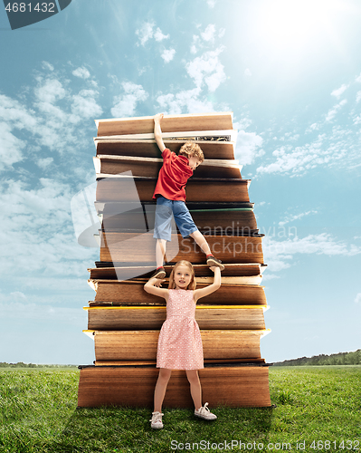 Image of Little girl and boy climbing on the tower made of big books