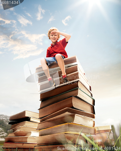 Image of Little boy sitting on the tower made of big books