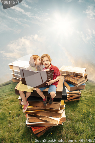 Image of Little girl and boy sitting on the tower made of big books